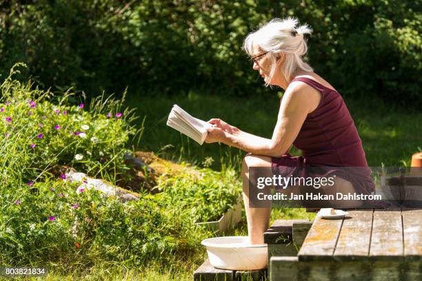 woman reading and having a footbath on cottage porch - tunic woman stock pictures, royalty-free photos & images