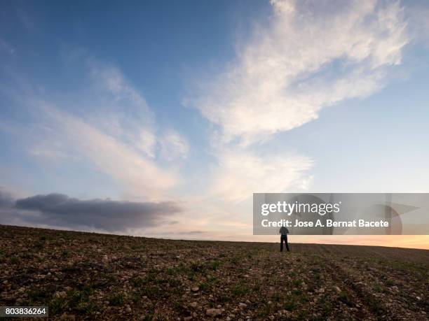 sunset with clouds of orange color on a ploughed field the spring , with the silhouette of a person contemplating the sky in the distance - campo arado fotografías e imágenes de stock