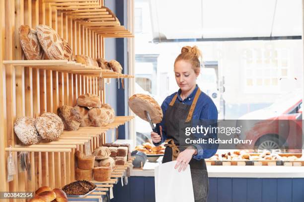 artisan baker putting bread loaf in to bag - bakery shelves stock pictures, royalty-free photos & images