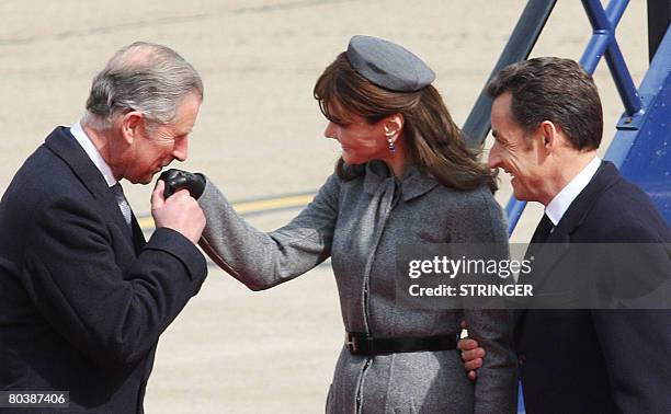 Britain's Prince Charles kisses the hand of Carla Bruni-Sarkozy as French President Nicolas Sarkozy looks on at Heathrow airport, west of London, on...