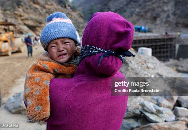 Nepali baby cries as her mother carries her while working on a road widening project, March 26, 2008 in Chuzom, Bhutan. Tens of thousands of migrant...