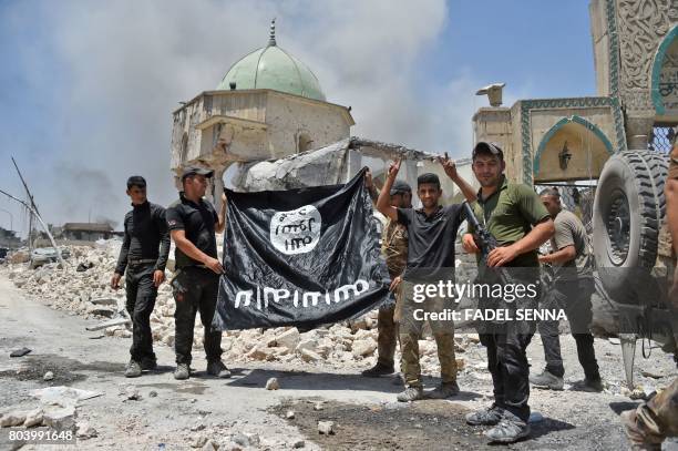 Member of the Iraqi Counter-Terrorism Service raises the victory gesture as others hold upside-down the black flag of the Islamic State group,...