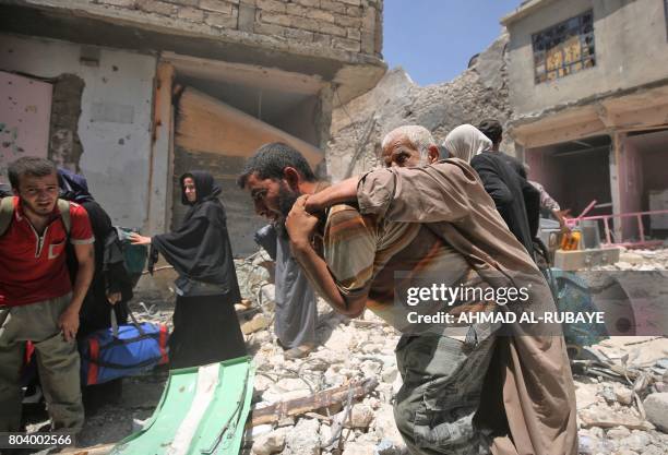 An Iraqi carries and elderly man while him and others evacuate from the Old City of Mosul on June 30 as Iraqi government forces continue their...