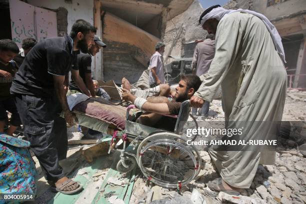 Iraqis help an injured man on a wheelchair evacuate from the Old City of Mosul on June 30 as Iraqi government forces continue their offensive to...