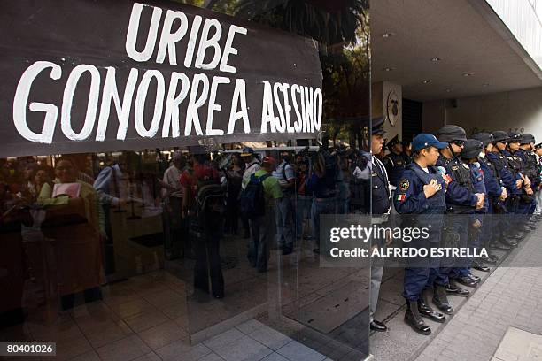 Police stand guard by a sign reading, "Uribe, Gonorrea Killer" at a protest for the Mexican university students who died during a Colombian Army...