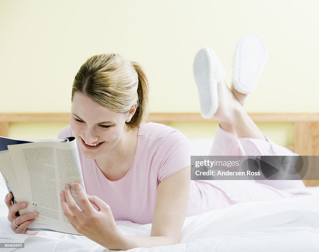 Woman lying down on bed with magazine