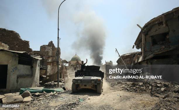 Member of the Counter-Terrorism Service seated on the top of an advancing humvee raises the victory gesture by the destroyed Al-Nuri Mosque in the...