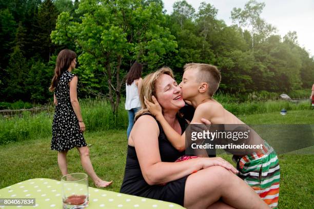 Young boy kissing mother at family reunion outdoors.