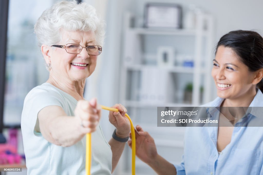 Senior patient smiles with therapist while using exercise band