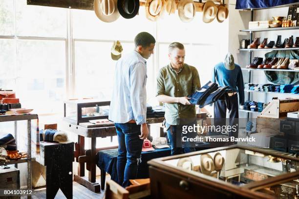 Shop owner explaining difference in denim jeans to customer in store
