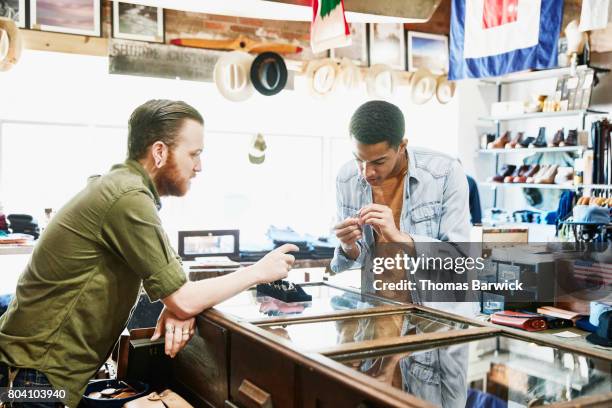 customer looking at ring while being helped by shop owner in mens boutique - juweliergeschäft stock-fotos und bilder