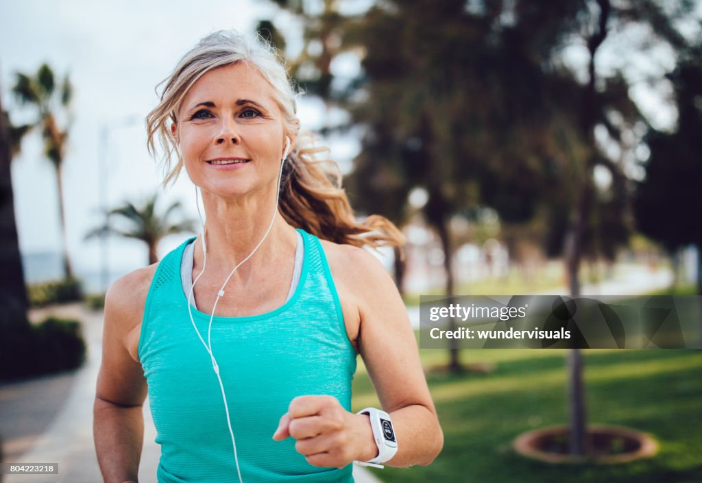 Active mature woman with headphones and smartwatch running in park