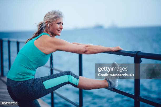 mulher de sênior ativa aquecendo à beira-mar para correr - older woman legs - fotografias e filmes do acervo