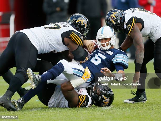 Davon Coleman and Ted Laurent and Adrian Tracy of the Hamilton Tiger-Cats sack Ricky Ray of the Toronto Argonauts during a CFL game at BMO Field on...