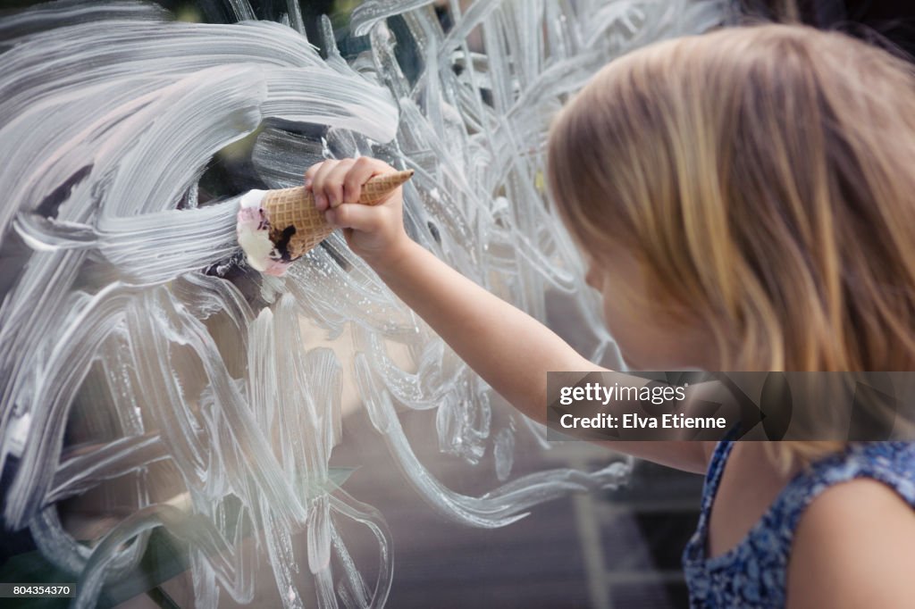 Child using ice cream in a cone, to paint a mess on a window