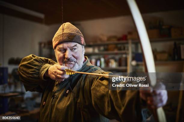 senior man holding handmade bow in workshop - arco y flecha fotografías e imágenes de stock