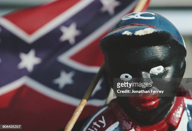 An American Civil War era miniature Stars and Bars Confederate battle flag is seen next to a Black Lawn Jockey statue during the 1998 NASCAR Winston...