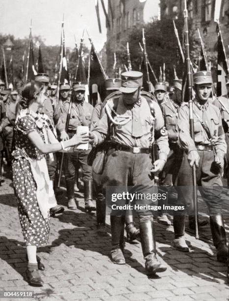 Fresh Drink from a Tender Hand Tastes Twice as Good', c1933 . A woman offers a drink to members of the SA marching in a parade. Founded in c1919, the...