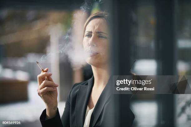 serious businesswoman smoking a cigarette at the window - cigarette smoking stockfoto's en -beelden