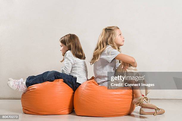 sisters sat back to back on beanbags - children only stock pictures, royalty-free photos & images