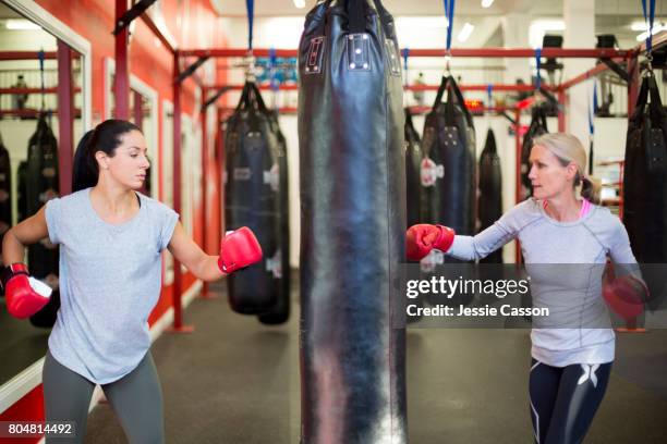 two female boxers punching the same punch bag in boxing gym - women's boxing stock-fotos und bilder