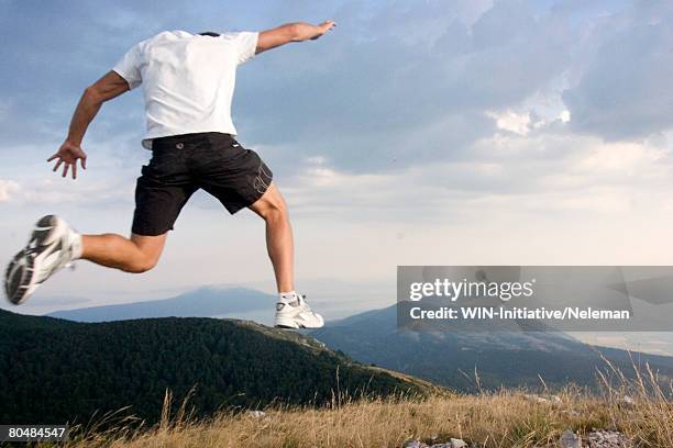 young man jumping up in the air in the mountains - running shorts fotografías e imágenes de stock
