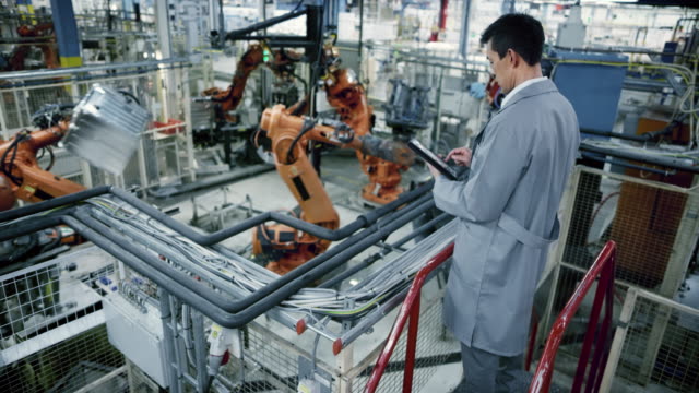 LD Male Asian engineer inspecting the work process of the robots performing their operations in the factory