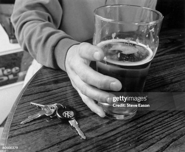 Man holding a pint of lager with his car keys next to it on a table in a British pub, 3rd July 1997.