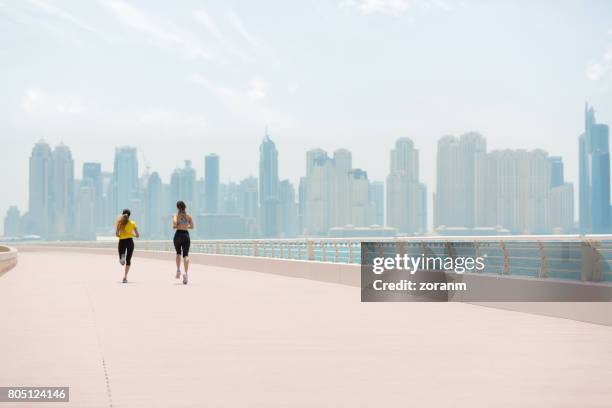frauen joggen mit stadtansicht im hintergrund - abu dhabi beach stock-fotos und bilder
