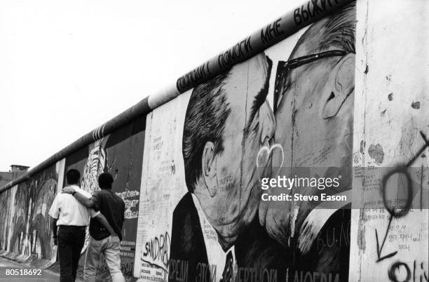 Gay couple strolling past graffiti on the Berlin Wall depicting German leaders Leonid Brezhnev and Erich Honecker sharing a kiss, August 1993.