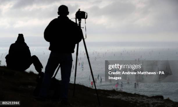 People take photos from the cliff tops as they watch hundreds of sailing boats make their way around the Isle of Wight close to the Needles as they...