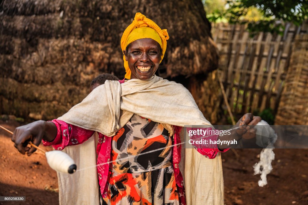 Mujer africana llevando a su bebé e hilado lana, África del este
