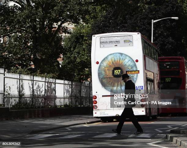 Man crosses the road behind a bus displaying Transport for London's new Drug Driving campaign poster, in Croydon, London.