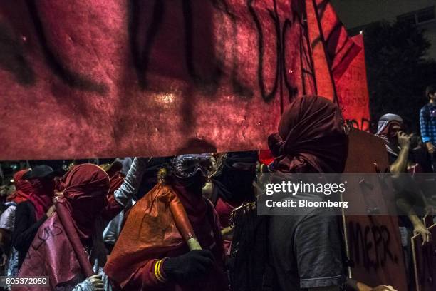 Masked demonstrators hold banners and flags during a general strike against labor and retirement reforms in Rio de Janeiro, Brazil, on Friday, June...