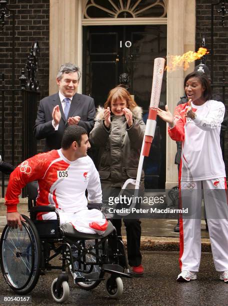 Paralympic powerlifter Ali Jawad takes the Olympic torch from Athlete Denise Lewis in Downing Street, accompanied by Prime Minister Gordon Brown and...
