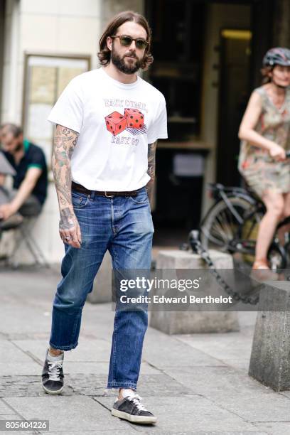 Guest wears sunglasses, a white t-shirt with printed red dice, blue denim cropped jeans, sneakers shoes, after Yohji Yamamoto show, during Paris...