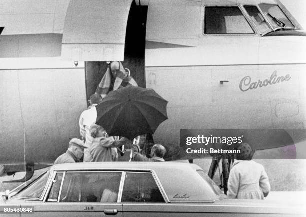 Former Ambassador Joseph P. Kennedy, wrapped with a shawl to keep the steady rain off him, is lifted aboard family plan Caroline for flight to Palm...