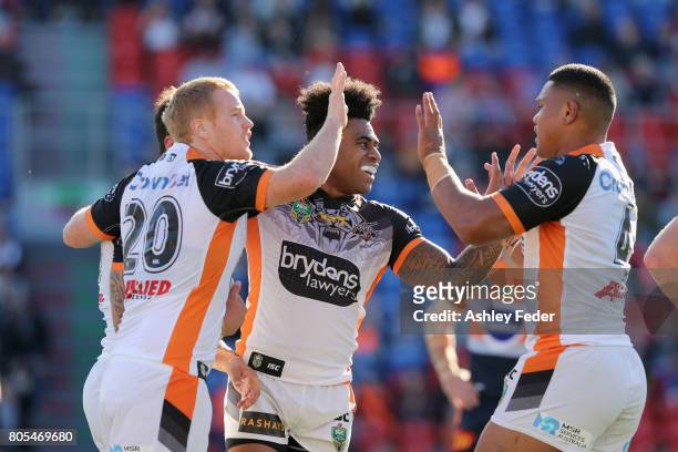 Malakai Watene-Zelezniak of the Tigers celebrates his try with team mates Kevin Naiqama and Joel Edwards during the round 17 NRL match between the...