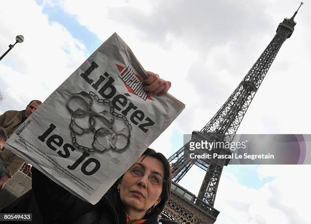 An unidentified Parisian holds the Liberation newpaper in front of the Eiffel Tower as the Olympic Torch Relay passes by on April 7, 2008 in Paris,...