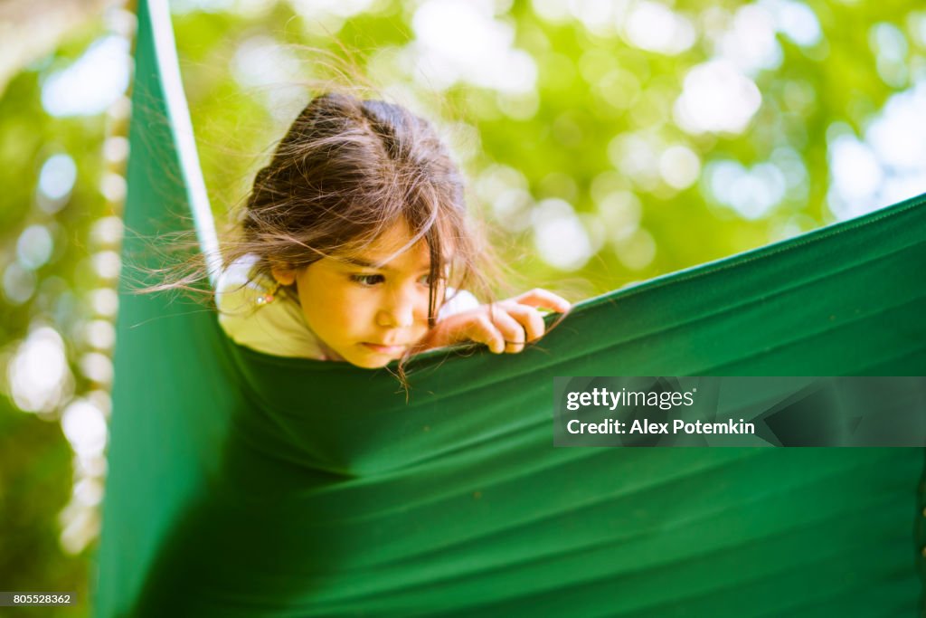 The little 5-years-old girl resting and have fun in the hammock in the park