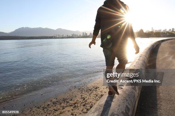 man balances on stone wall in waterfront area - blue shorts stock-fotos und bilder