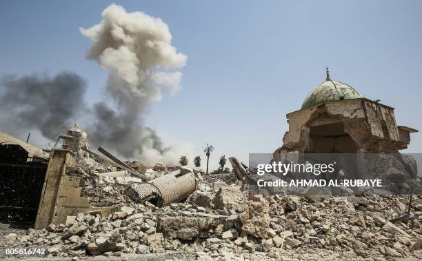 Smoke billows in the background behind the remains of the destroyed leaning minaret, known as the "Hadba", and Al-Nuri Mosque in the Old City of...