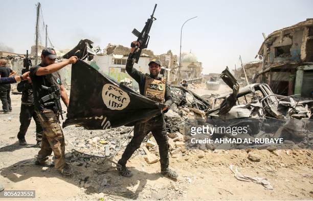 Members of the Iraqi Counter-Terrorism Service cheer as they carry upside-down a black flag of the Islamic State group, with the destroyed Al-Nuri...