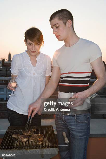 a young couple having a barbeque on a rooftop terrace - couple grilling stock pictures, royalty-free photos & images