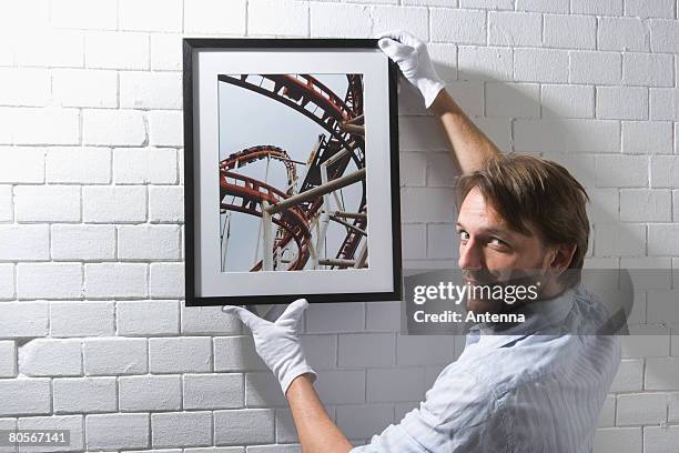 a man hanging a framed photograph on a wall - putting gloves stock pictures, royalty-free photos & images
