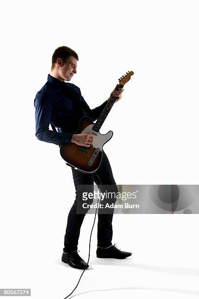 studio shot of a man playing an electric guitar - guitarrista fotografías e imágenes de stock