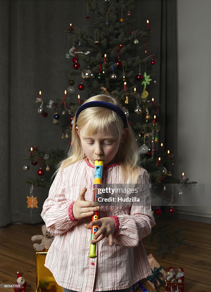 A girl playing a recorder in front of a Christmas tree