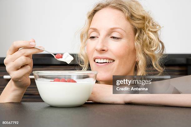 a woman holding a spoon of yogurt and raspberries up to her mouth - yogurt spoon stock-fotos und bilder