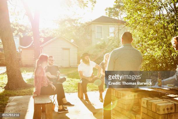 group of friends sitting in backyard on sunny summer evening - garden party stock-fotos und bilder