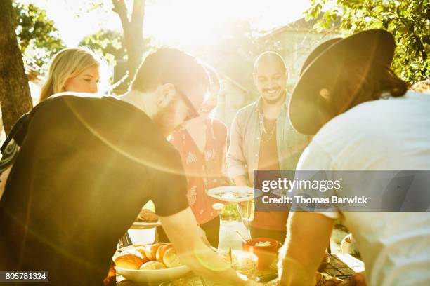 smiling friends dishing up food in backyard on summer evening - barbecue photos et images de collection